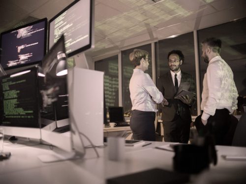 Three talented coders gathered together at dim open plan office and presenting their point of view concerning brand new computer app
